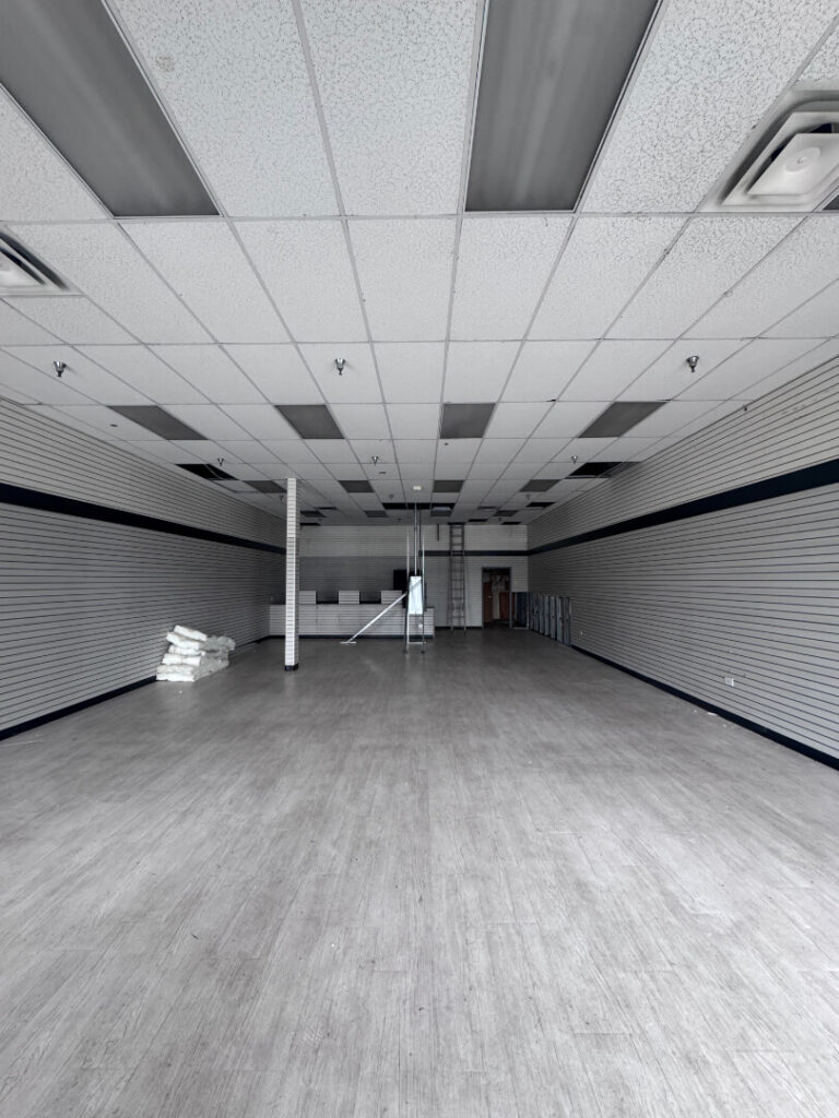 Construction workers dismantle a building's remnants, clearing debris with shovels and machinery under a blue sky.